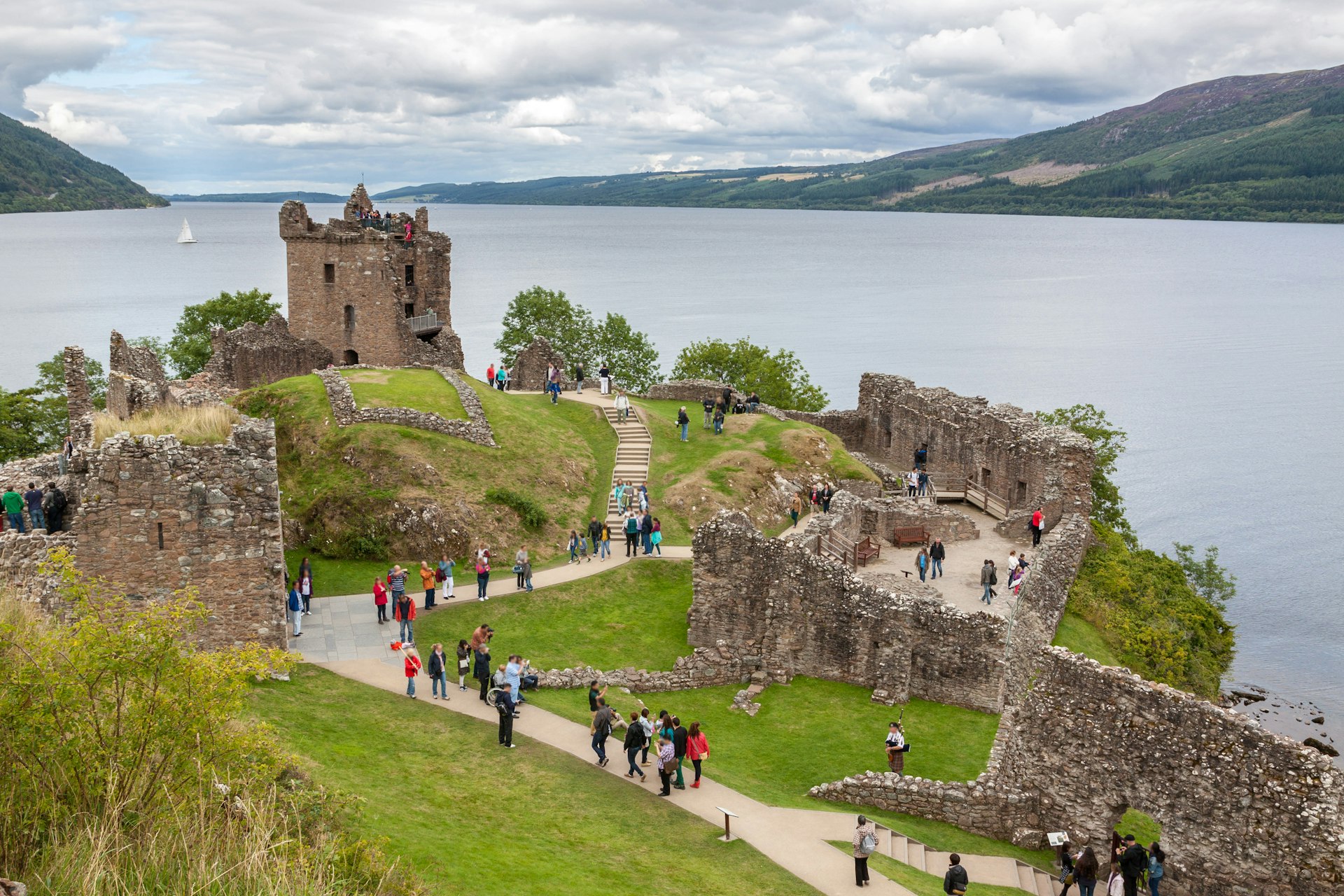 An aerial shot of a ruined castle with many visitors on the edge of a loch
