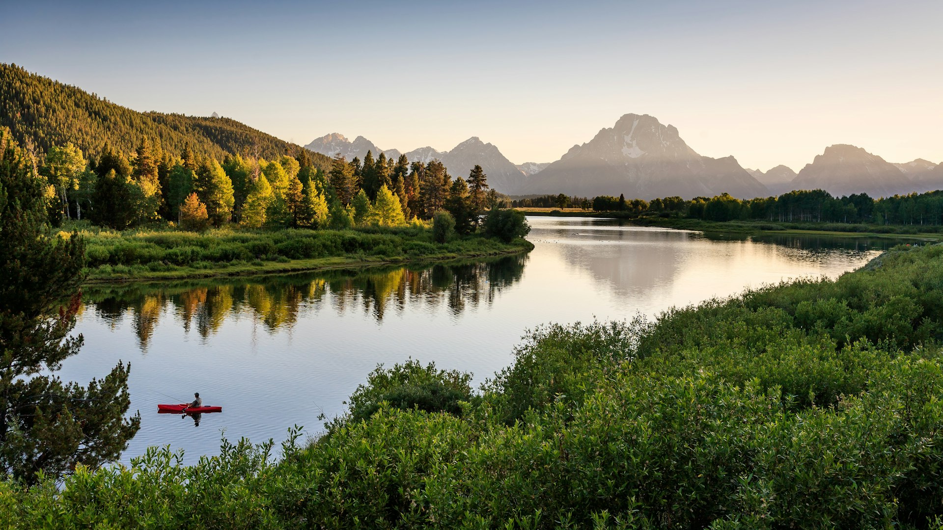 A wide shot of a fisherman in a kayak on the Snake River in Grand Teton National Park