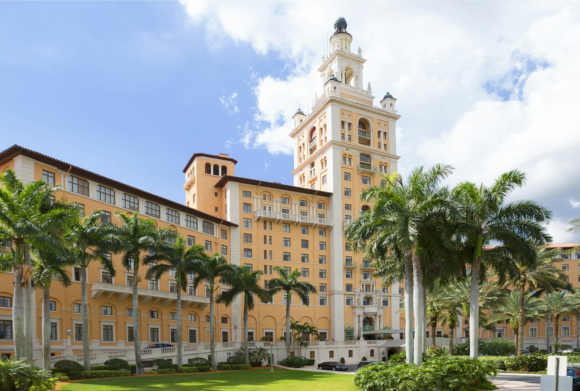 A huge pastel-colored hotel building with a central pointed tower in tropical gardens
