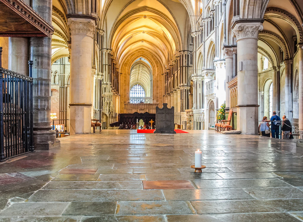 A single candle burns on the floor of a huge stone cathedral building with a vaulted ceiling