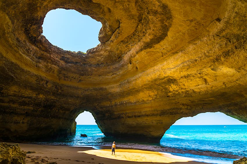 shutterstockRF_566989303.jpg Um homem solitário está em uma caverna em Penang, Portugal. Penang possui uma grande caverna marítima, com um grande buraco no telhado que permite que a luz solar incida sobre a praia no seu interior.