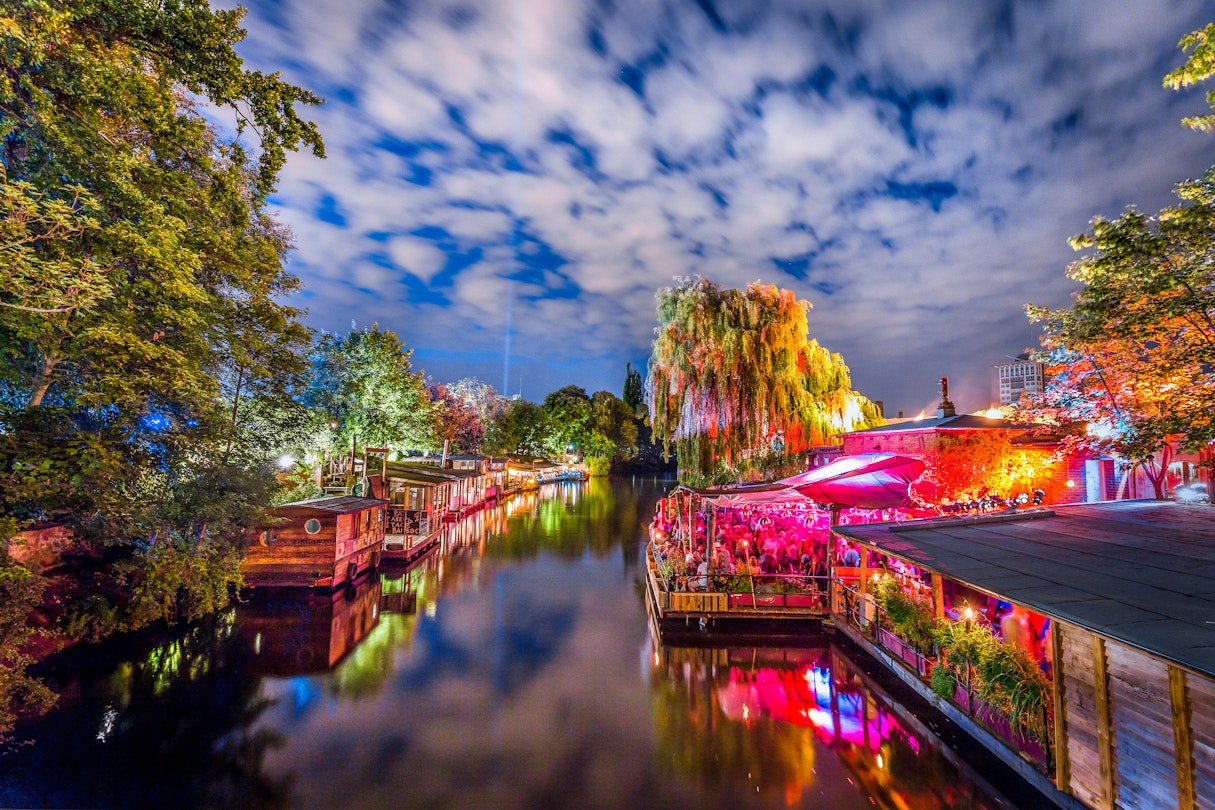Panoramic view of young people partying in an open-air outdoor club at famous Flutgraben water canal on a beautiful warm summer night with moving clouds in Berlin Kreuzberg, Germany