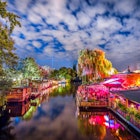 Panoramic view of young people partying in an open-air outdoor club at famous Flutgraben water canal on a beautiful warm summer night with moving clouds in Berlin Kreuzberg, Germany
