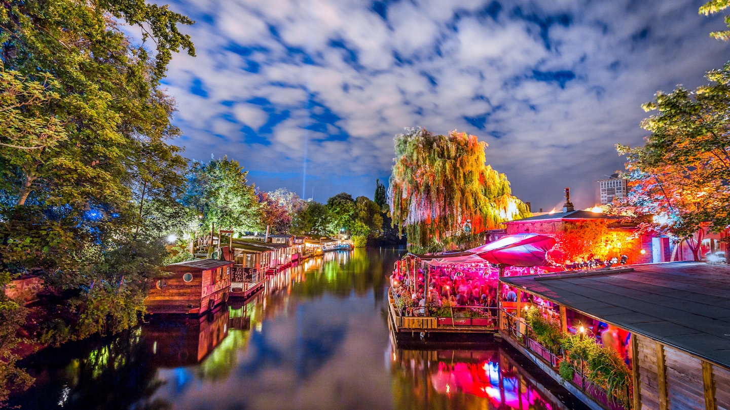 Panoramic view of young people partying in an open-air outdoor club at famous Flutgraben water canal on a beautiful warm summer night with moving clouds in Berlin Kreuzberg, Germany