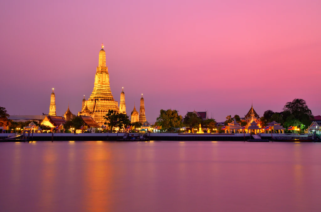 Bathed in golden light, Wat Arun sits against a pink sky at sunset in Bangkok, Thailand.