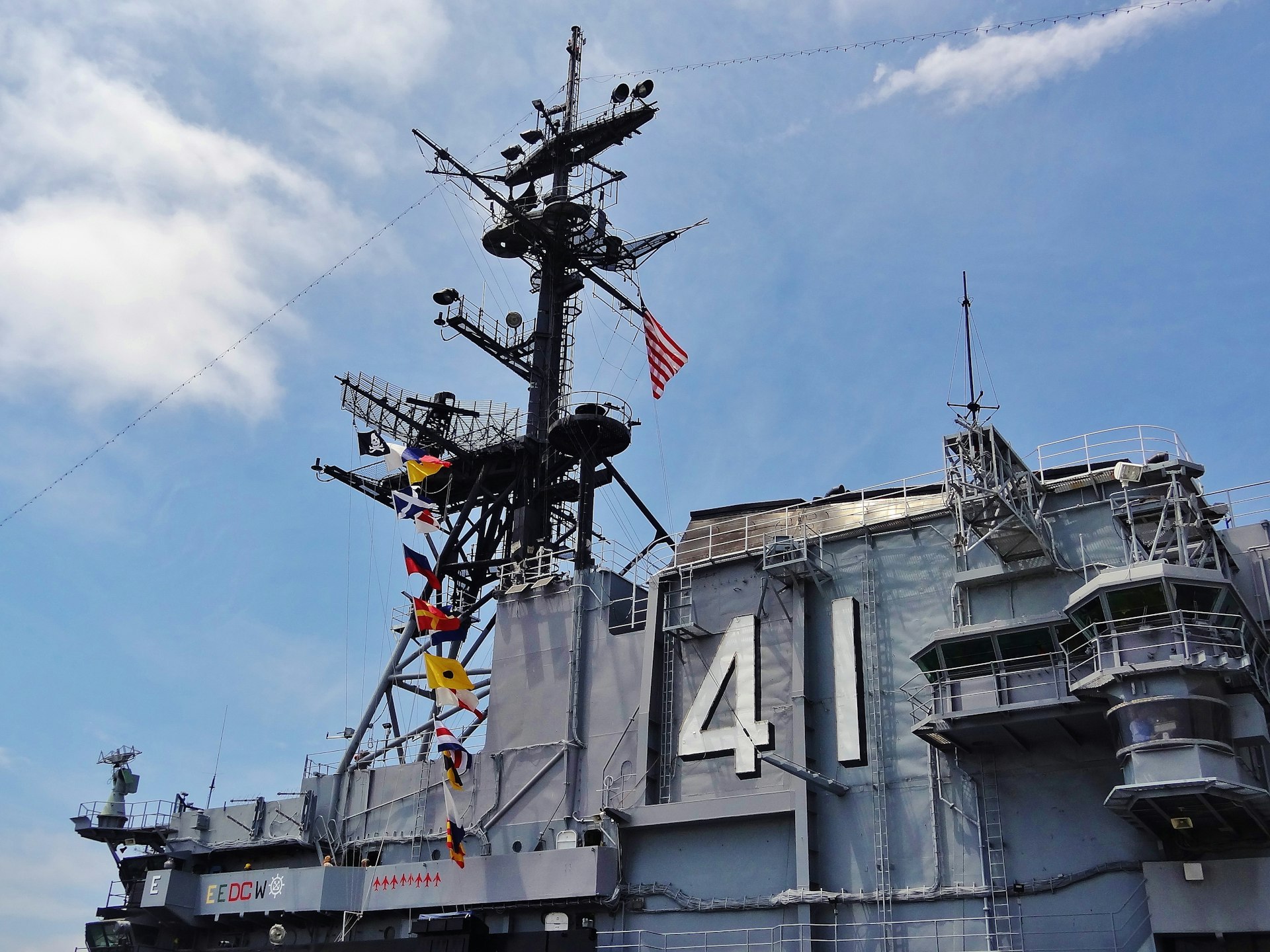 A large grey warship with a communications turret displaying several flags