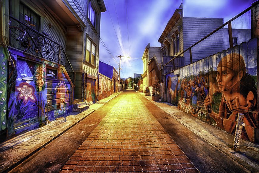 An alleyway at dusk has murals painted along the walls on each side