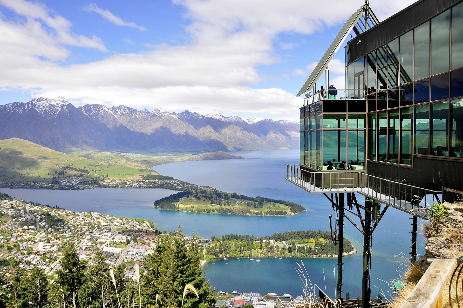 The large glass building sits on a high hill overlooking the Queenstown skyline of snow-capped mountains and a large lake with chunks of green jutting out of the water.