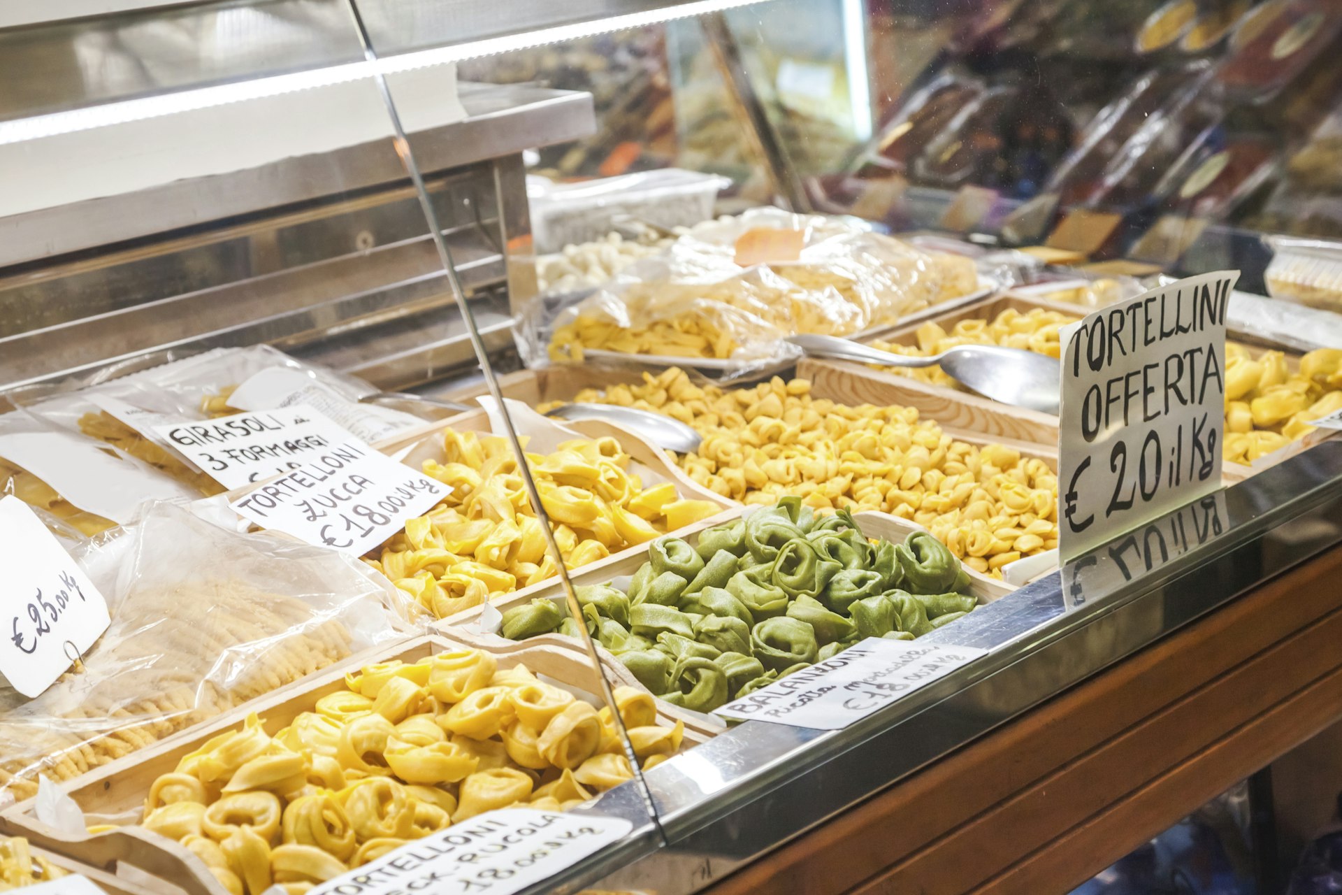 A store in Bologna selling vast quantities of pasta, including tortellini and tortelloni. The pasta is displayed next to prices, written in Italian.