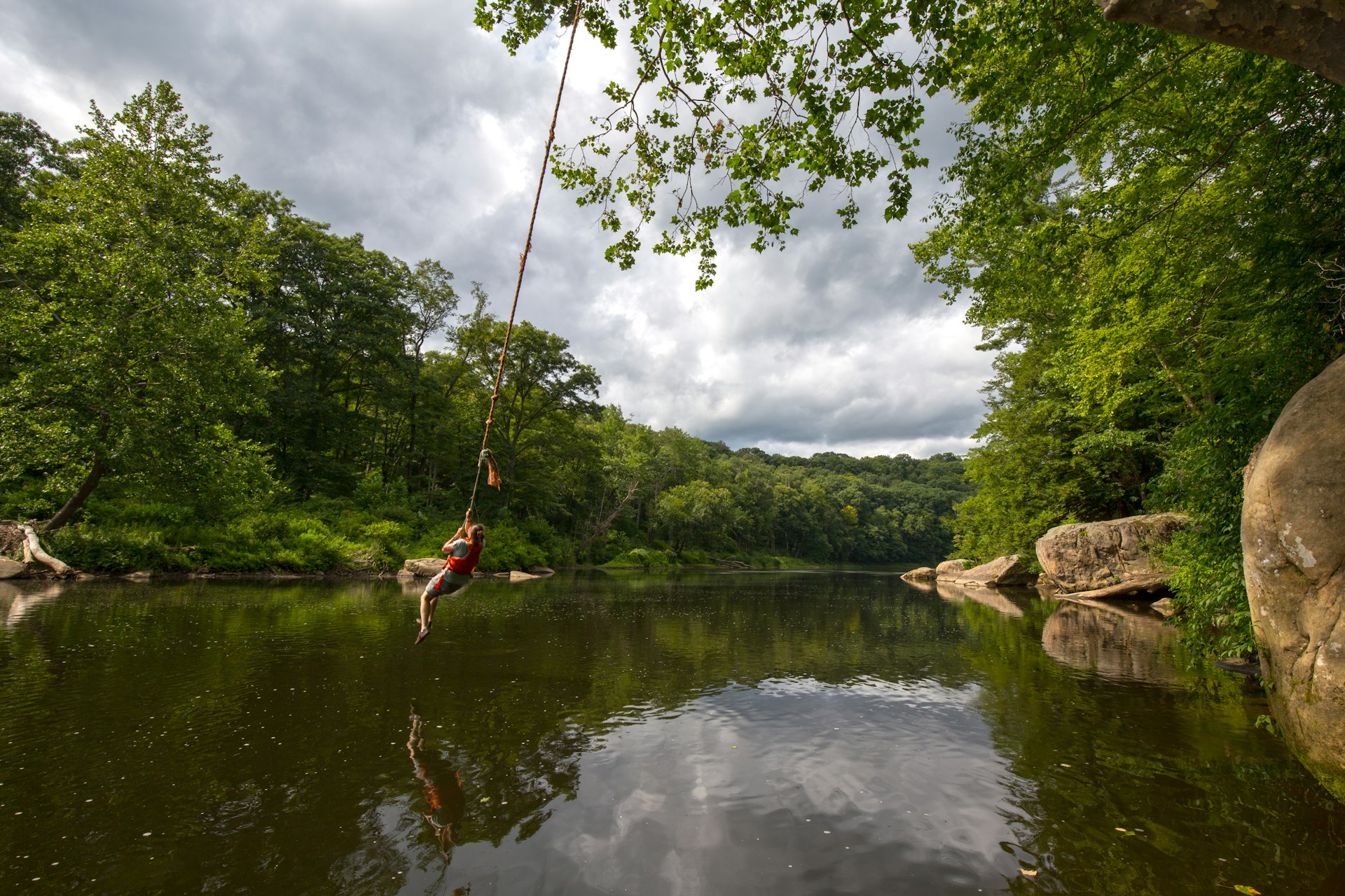 A person swings off a rope swing over the Clarion River surrounded by trees on a hot summer day. 