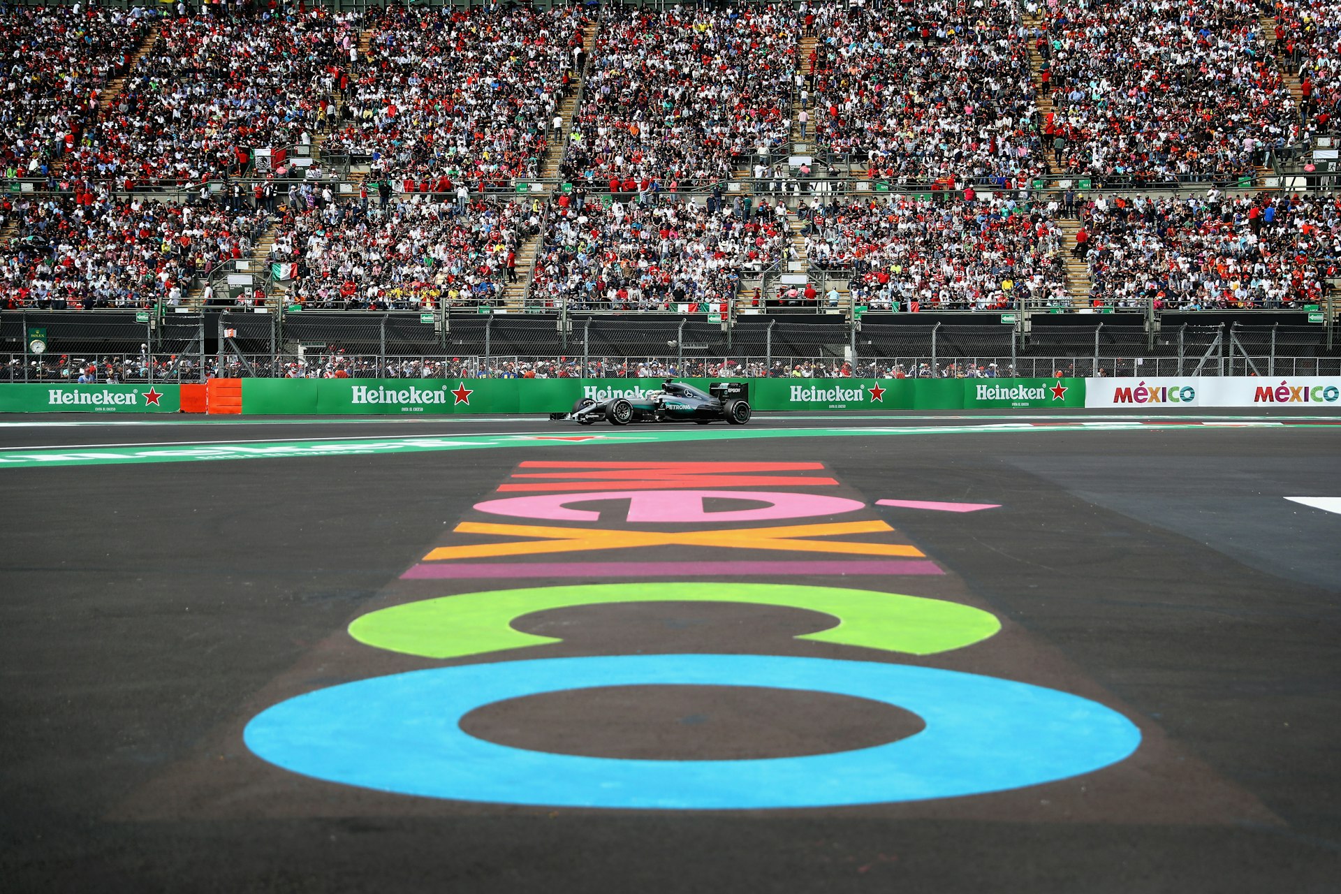 A Formula 1 racing car on a track with thousands of spectators in the stands watching on