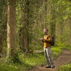 African American man standing on path in forest holding binoculars
