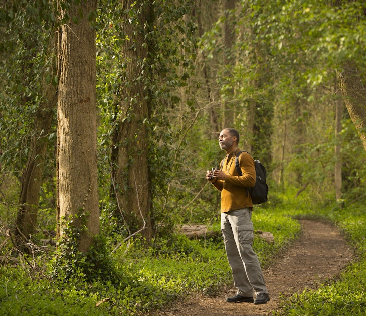 African American man standing on path in forest holding binoculars
