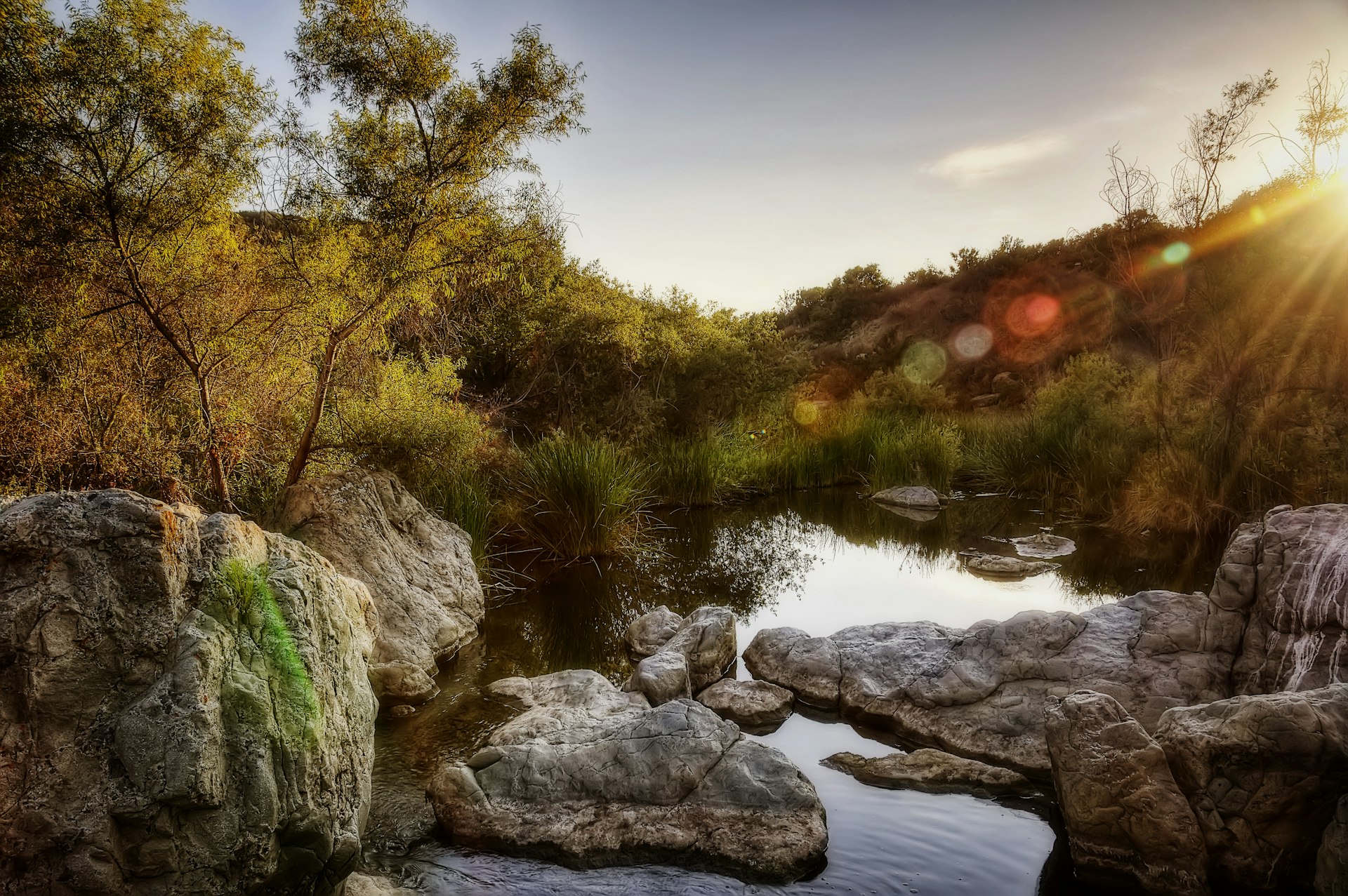 A waterhole surrounded by large boulders with a setting sun