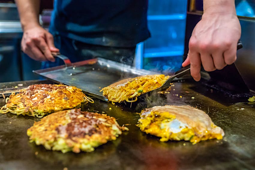 A chef cooking a cabbage and egg-based pancake on a hot plate