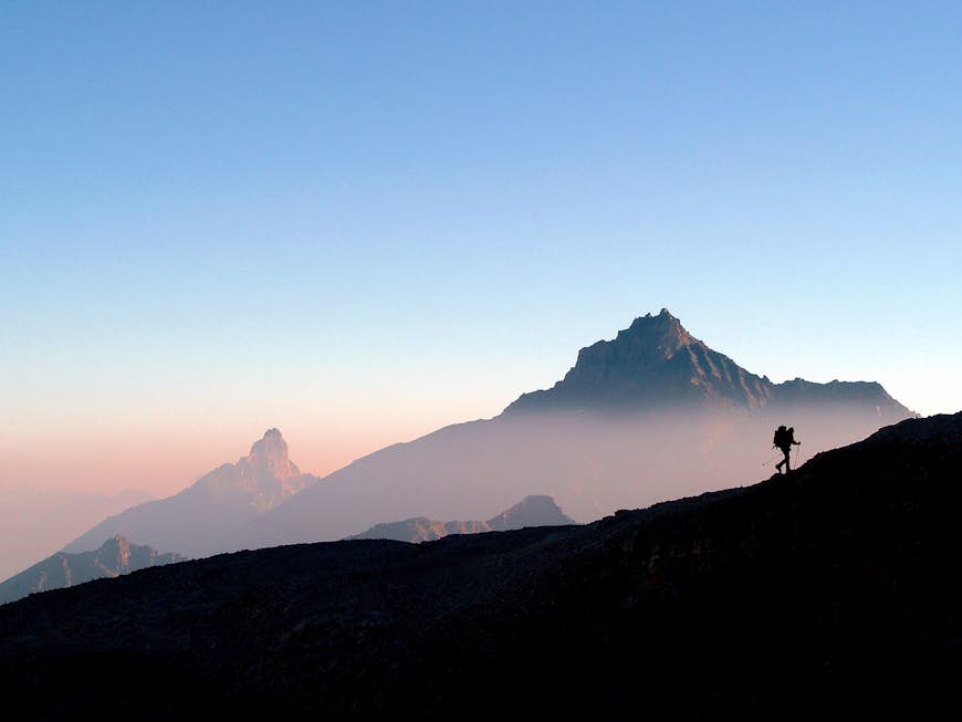 Siluett av en vandrare med en ryggsäck som klättrar på en ås i bergen i Gran Paradiso nationalpark under soluppgången