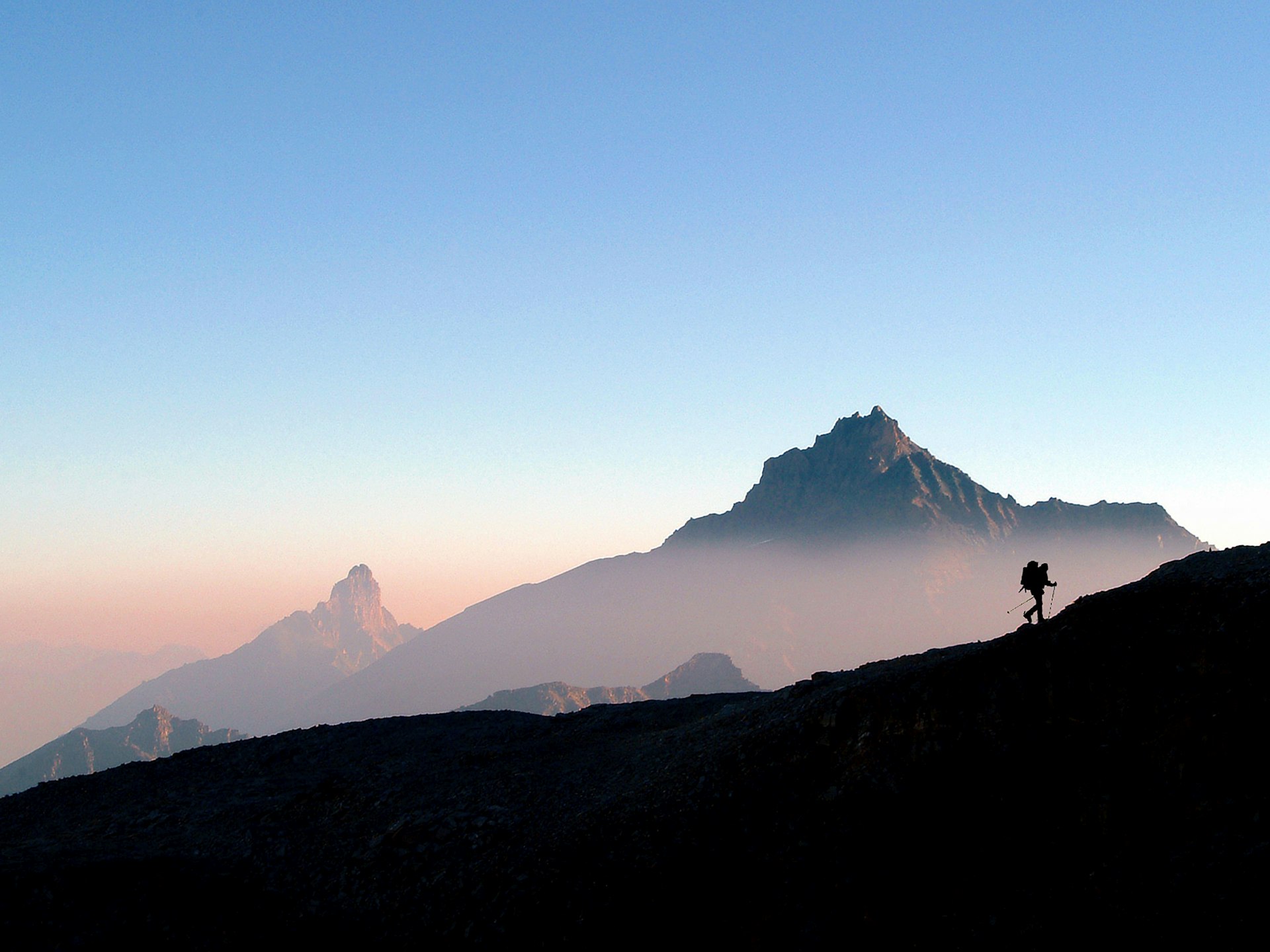Silhouette of a hiker with a backpack climbing a ridge in the mountains of Gran Paradiso National Park during sunrise