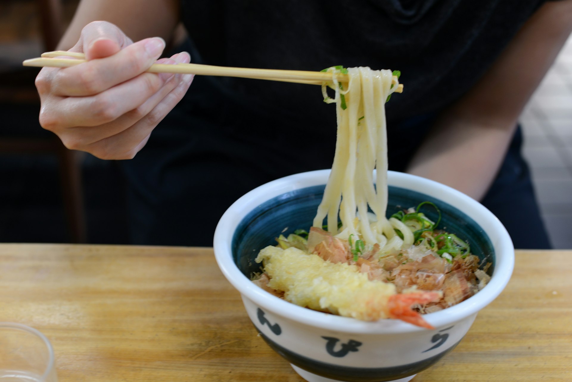 Chopsticks lifting noodles above a bowl 
