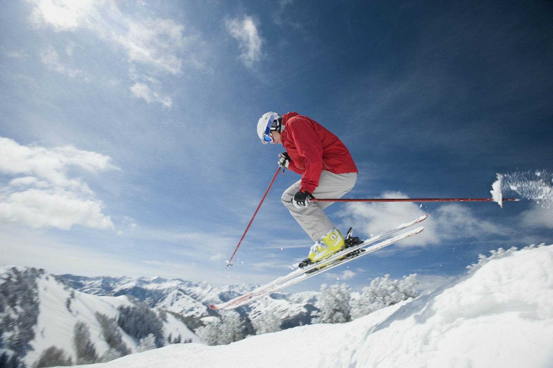 A man in a bright red jacket and goggles, getting air as he skis downhill