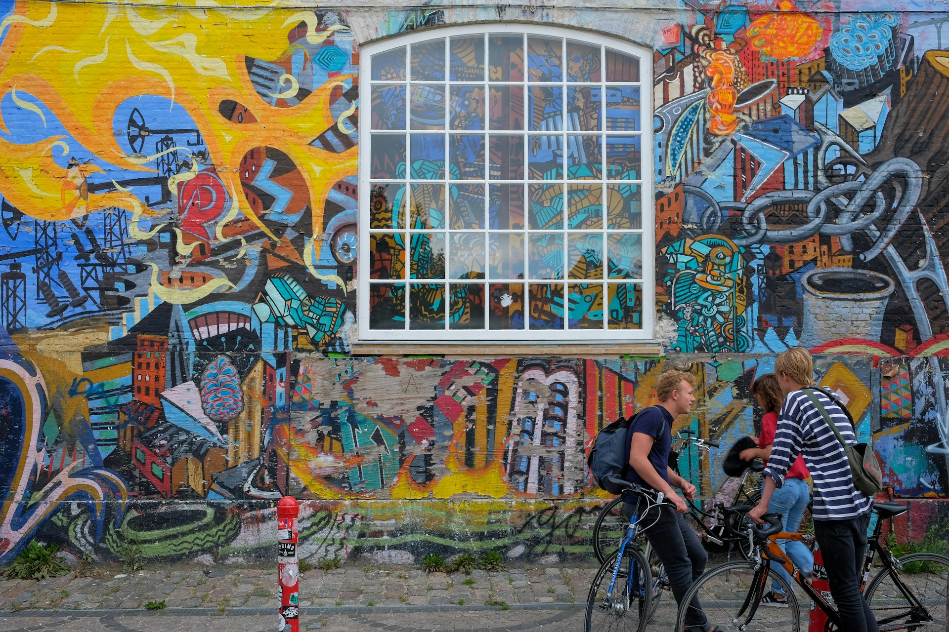 Young people with bikes stand in front of a graffiti wall in Christiania, Copenhagen