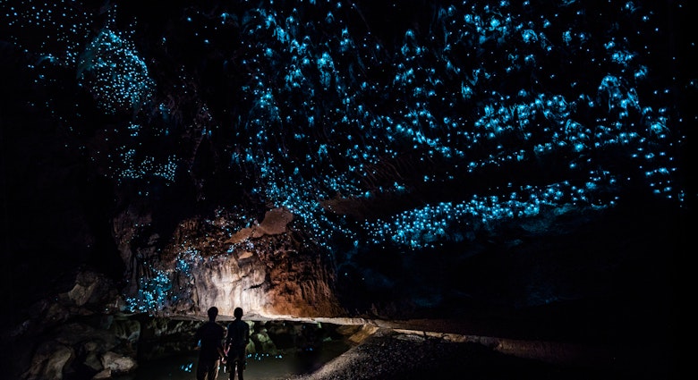 Two people explore the glowworm cathedral at the end of Waipu Cave in New Zealand.