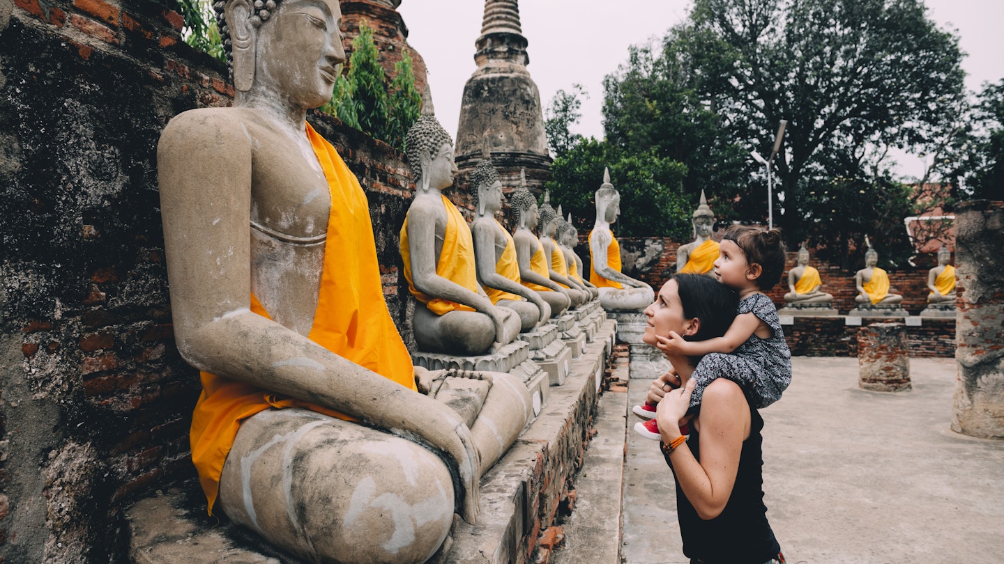 Ayutthaya, Buddha statues in a row in Wat Yai Chai Mongkhon, mother and daughter in front of a Buddha statue.