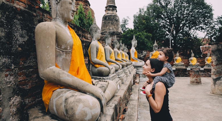 Ayutthaya, Buddha statues in a row in Wat Yai Chai Mongkhon, mother and daughter in front of a Buddha statue.