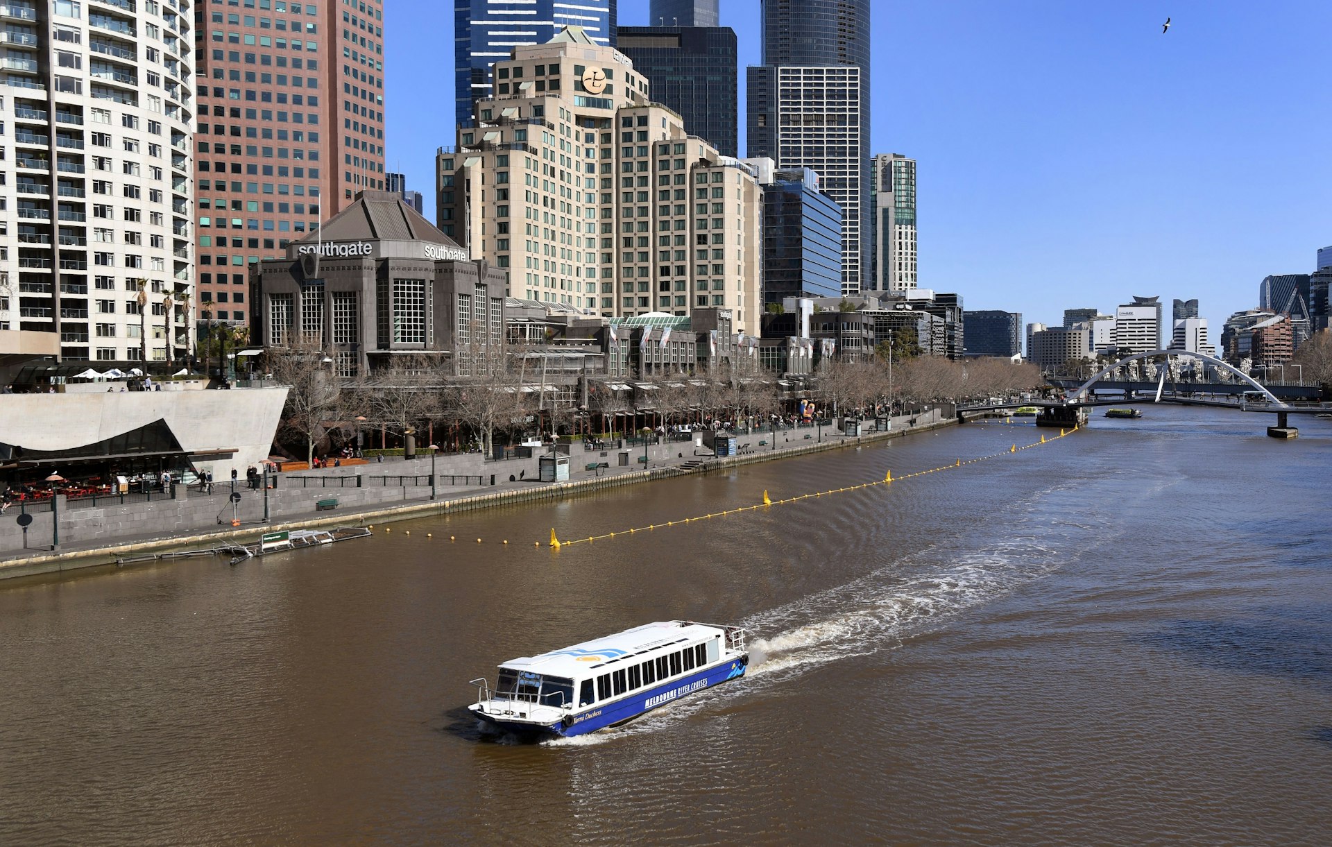 A ferry transports tourist down Melbourne's wide Yarra River. In the background, several high-rise buildings are visible.