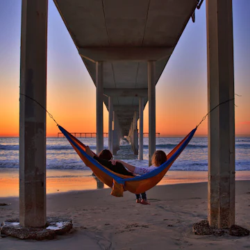 Ocean Beach, California - December 12, 2017: Romantic couple in a hammock under the Ocean Beach Pier watching a colorful sunset.