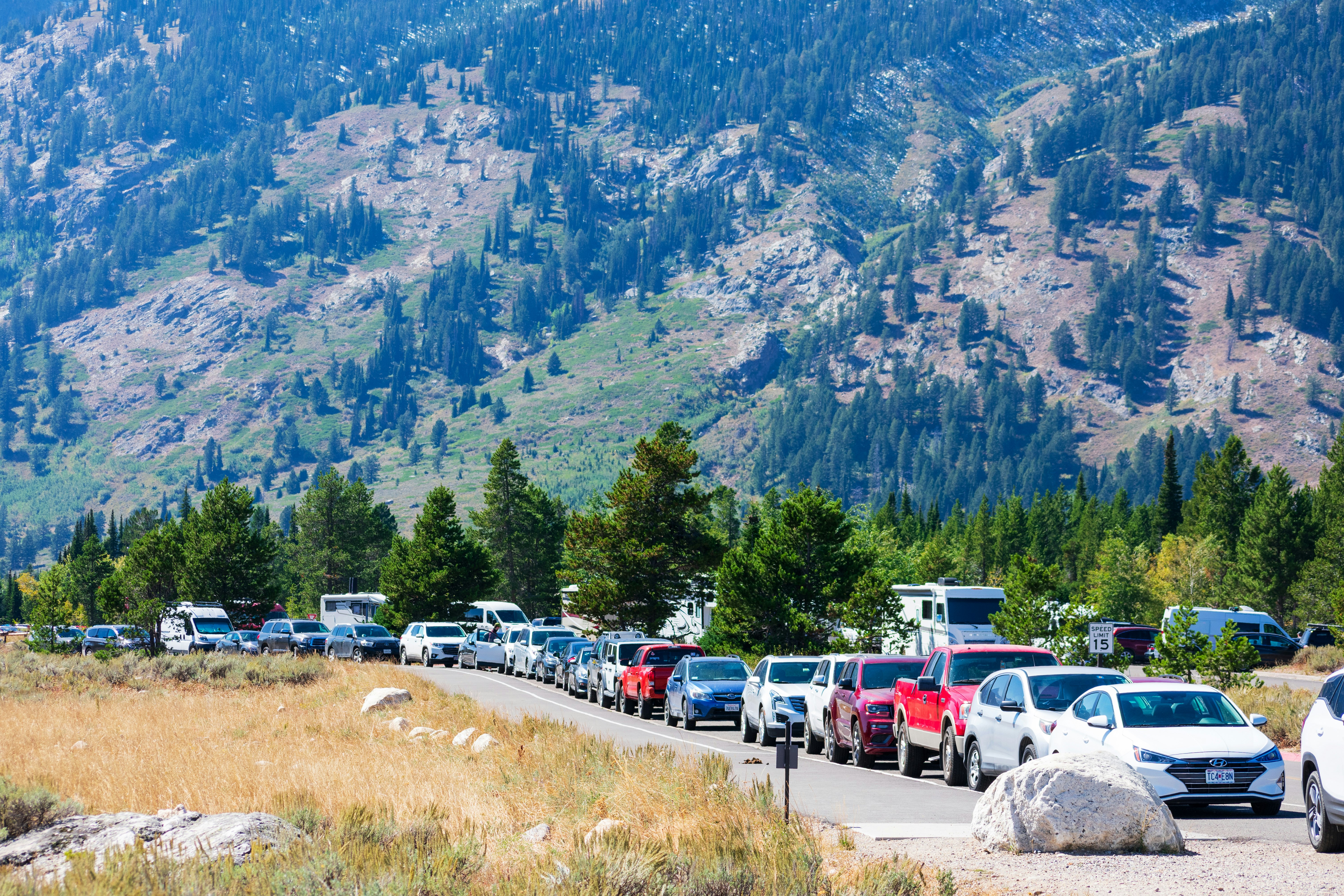 A large line of cars parked bumper to bumper on the road leading to Grand Teton National Park.