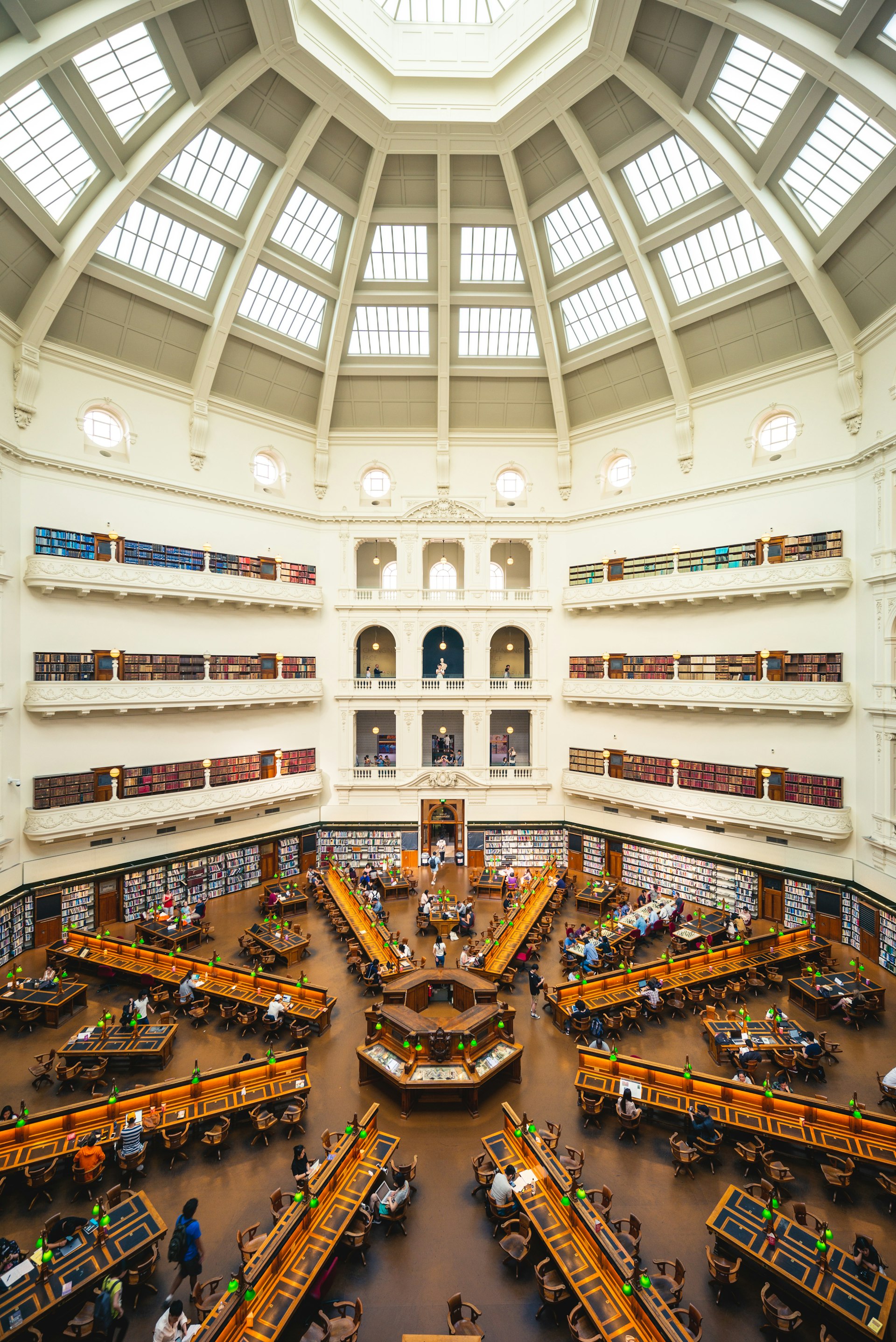 A vertical profile view of the La Trobe Reading Room at the State Library of Victoria, Melbourne. The room has a high, dome ceiling and a number of old-looking desks, where people sit to study and read.