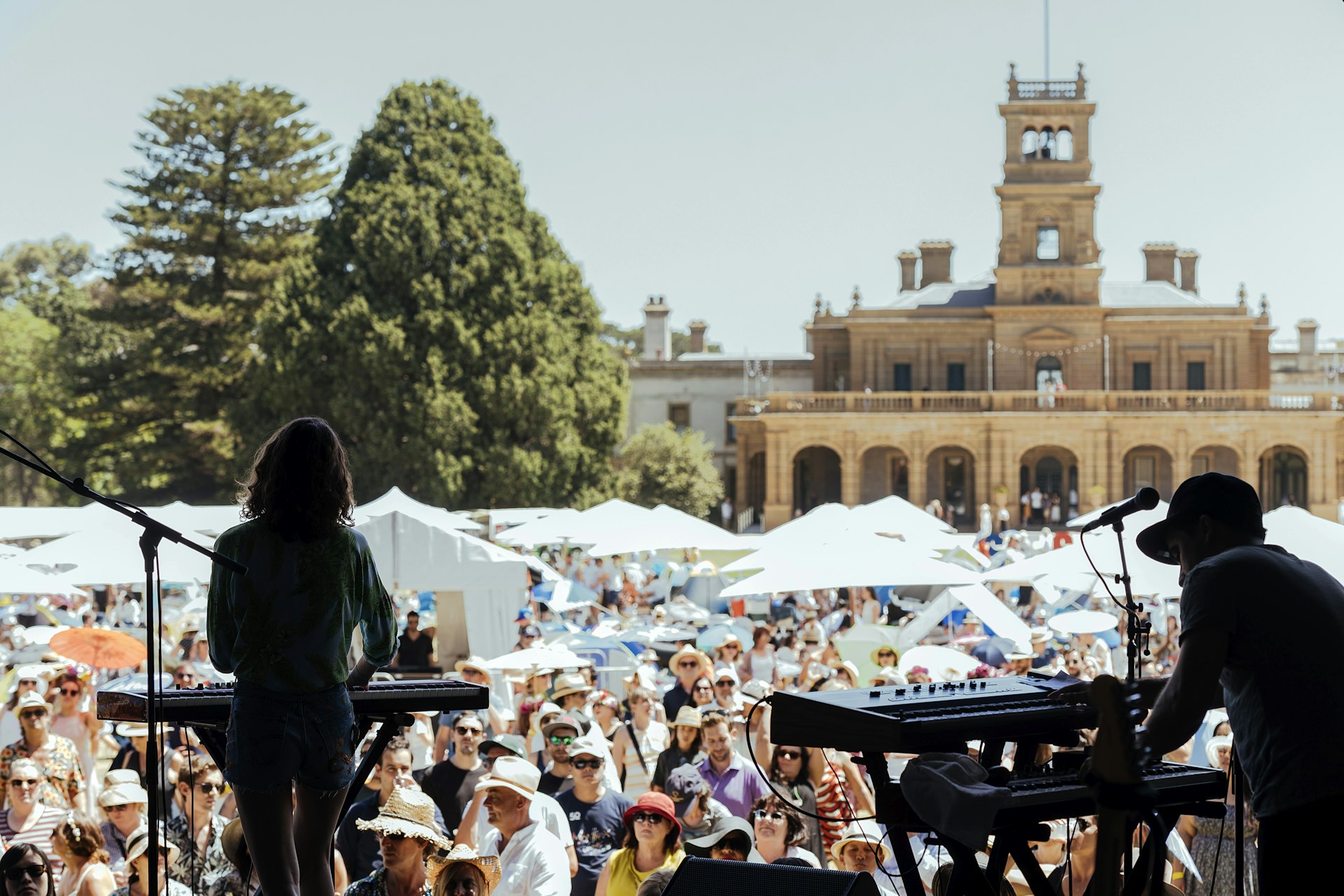 Cléa Vincent performing as part of So Frency So Chic at Werribee Park. The image is taken from behind the artist on stage, with a large crowd visible in the grounds. Behind them is a grand old building.