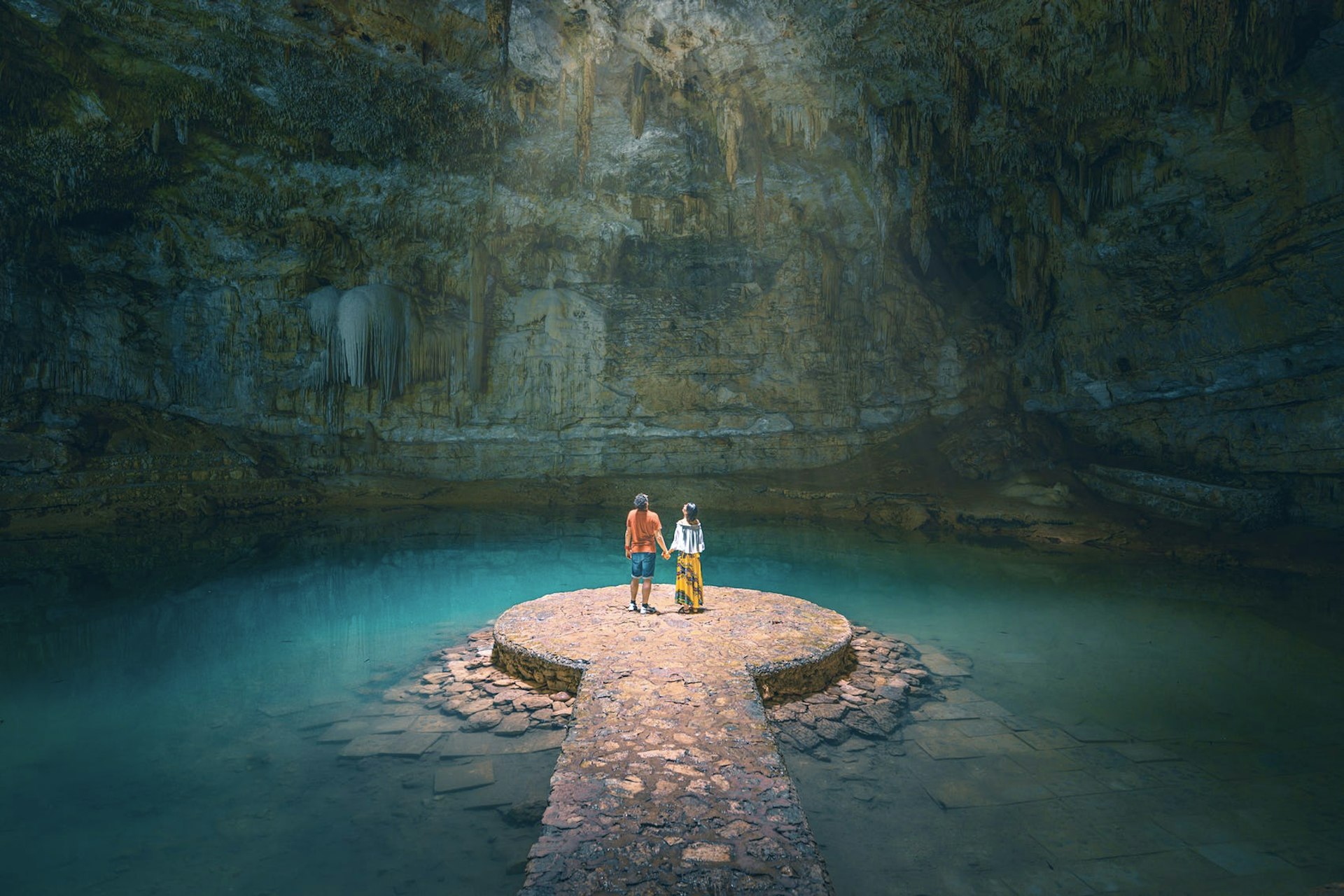 A couple hold hands in a sunlit cavern in Yucatan