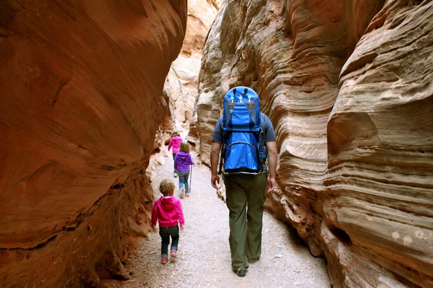 An adult walks through a slot canyon with two kids