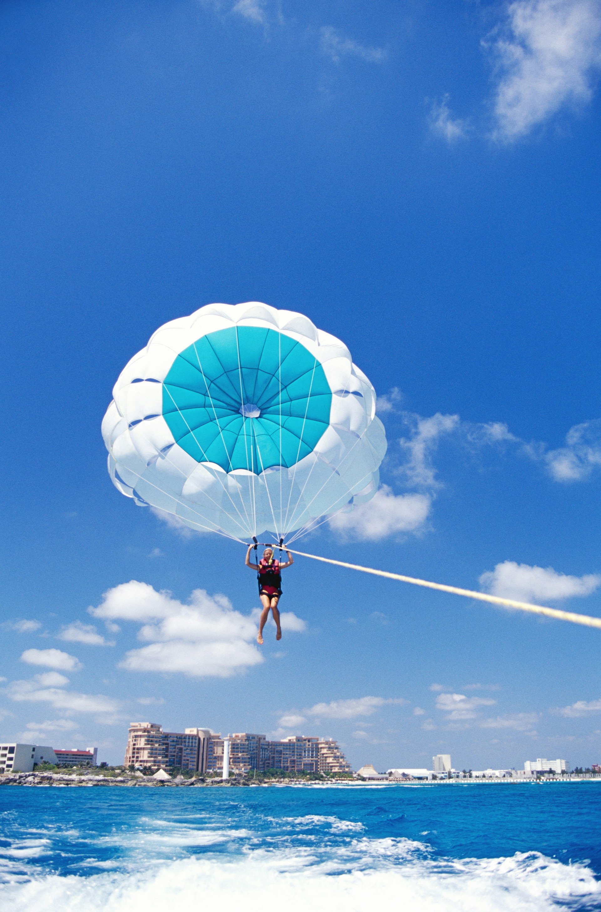 A person attached to a parachute flies high above the ocean towed by a boat