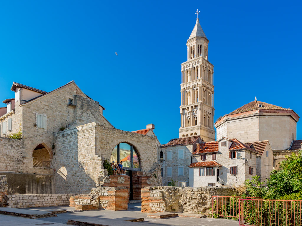A white bell square tower rises above a Roman city