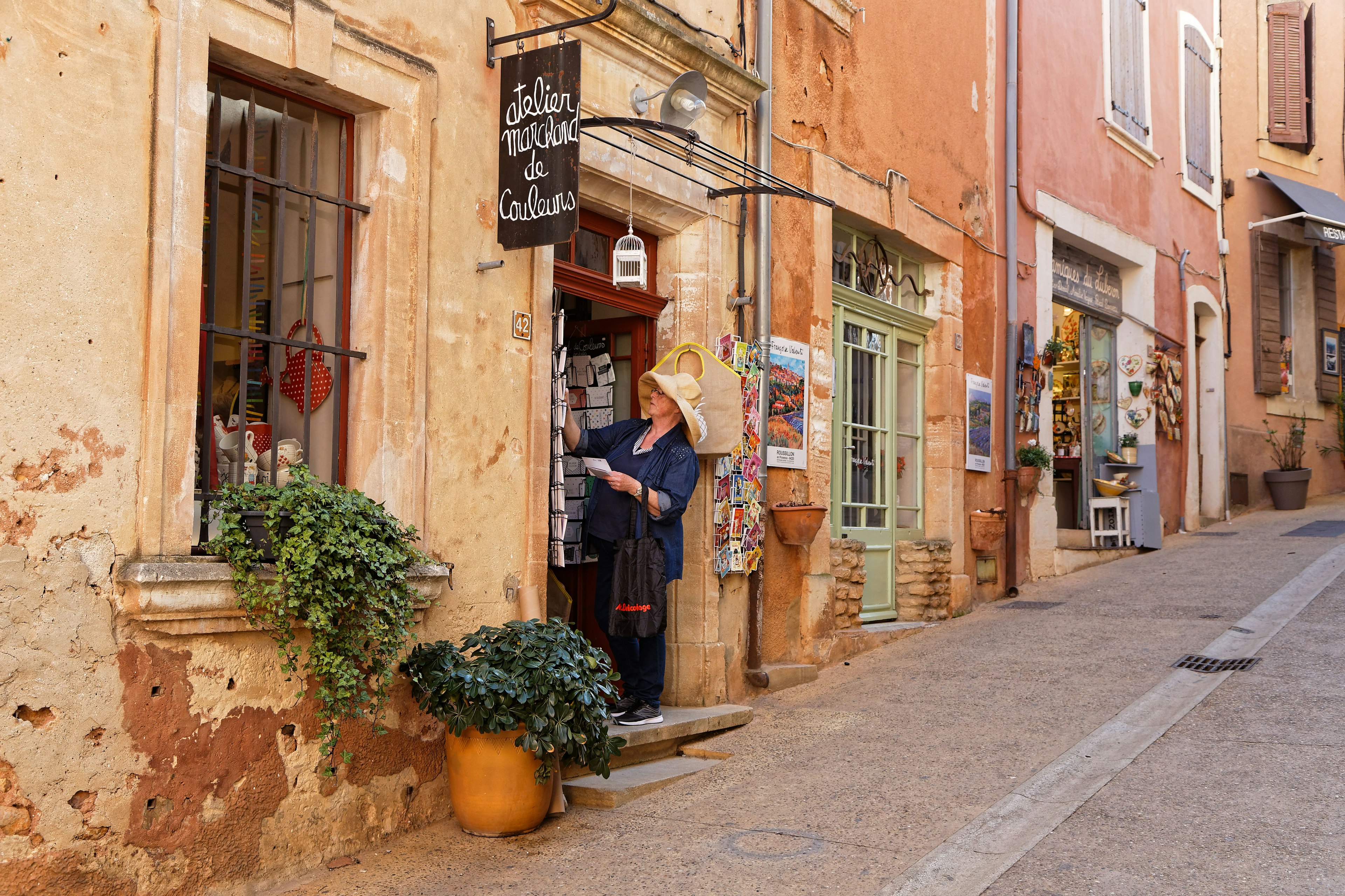 A woman looks at items on display at a gift store on a narrow street