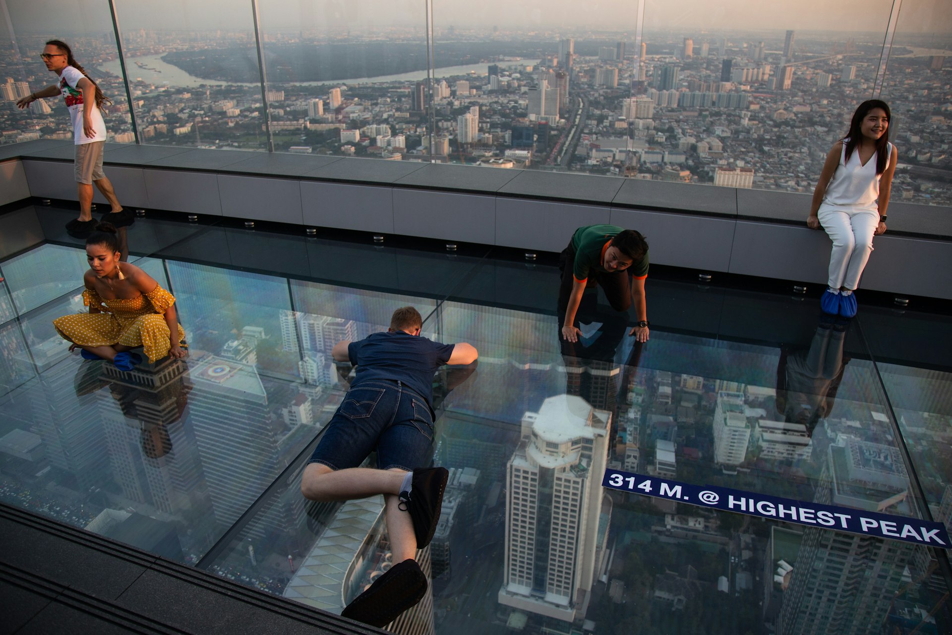 Visitors sit and lie on the glass floor at the rooftop of the King Power Mahanakhon building in Bangkok as the lights of the city skyline, some way below, glitter.