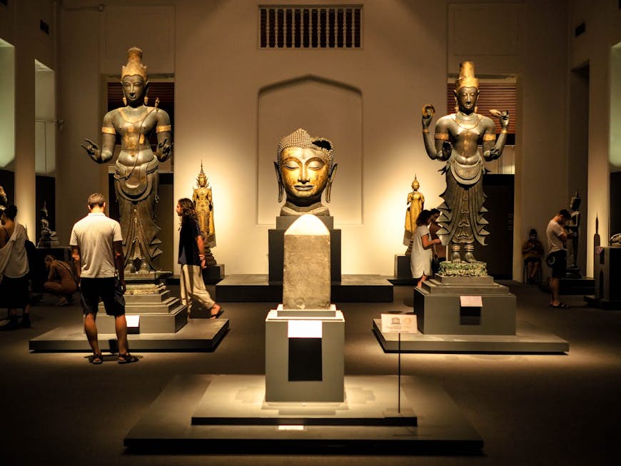 Tourists look at Thai art and artefacts which are lit up by lights in the National Museum in Bangkok, including giant sculptures of heads