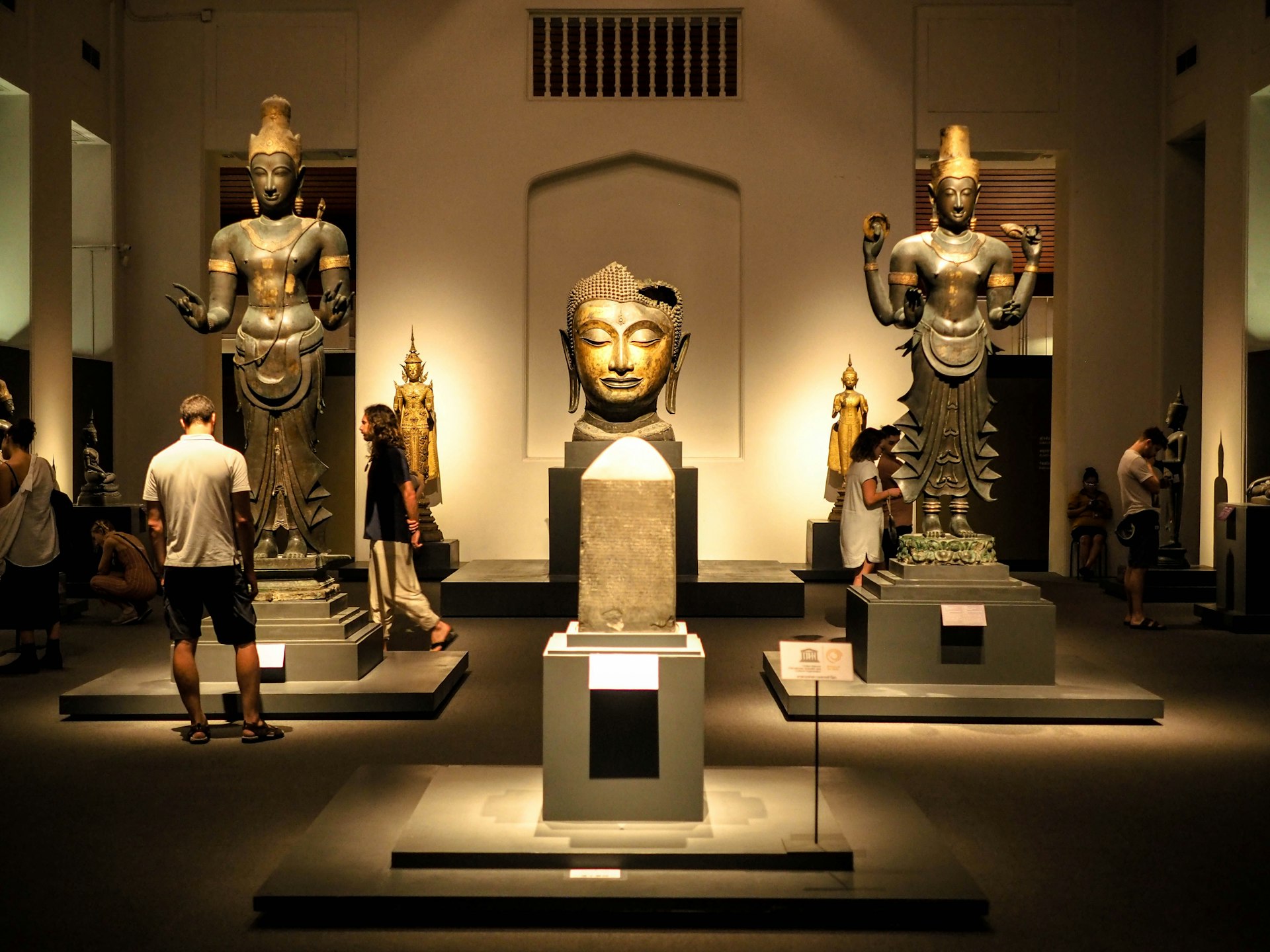 Tourists look at Thai art and artefacts which are lit up by lights in the National Museum in Bangkok, including giant sculptures of heads