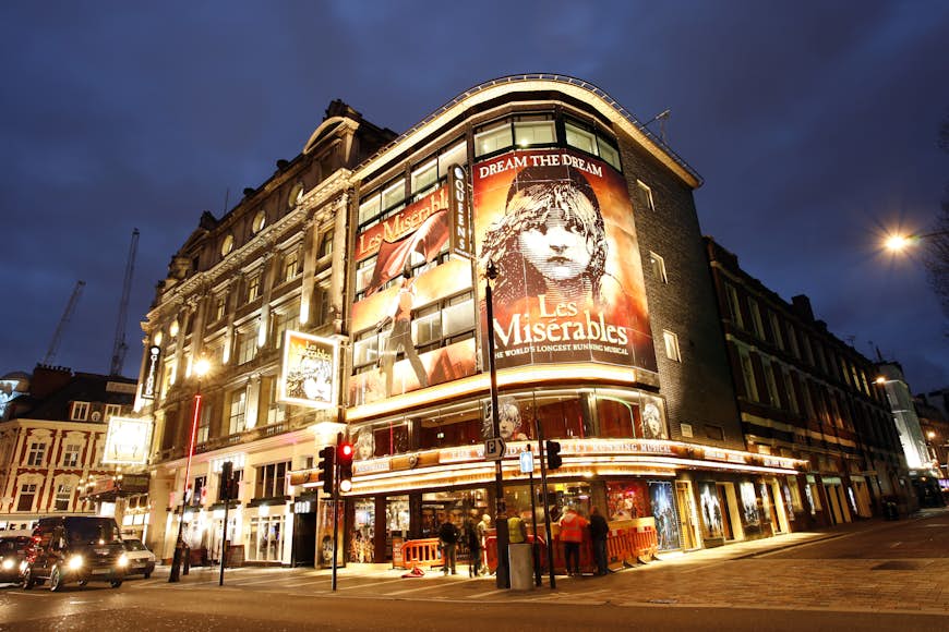 A London theater on the corner of two streets. A huge poster of a child's face advertises the play "Les Miserables".