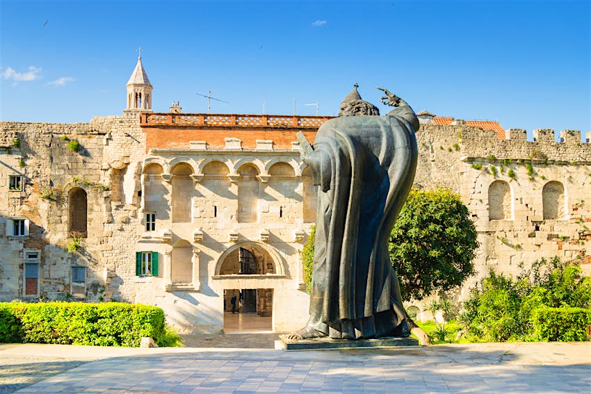 Golden Gate, Diocletian's Palace, Split A doorway in a long white-brick wall with a huge metal sculpture of a figure facing it