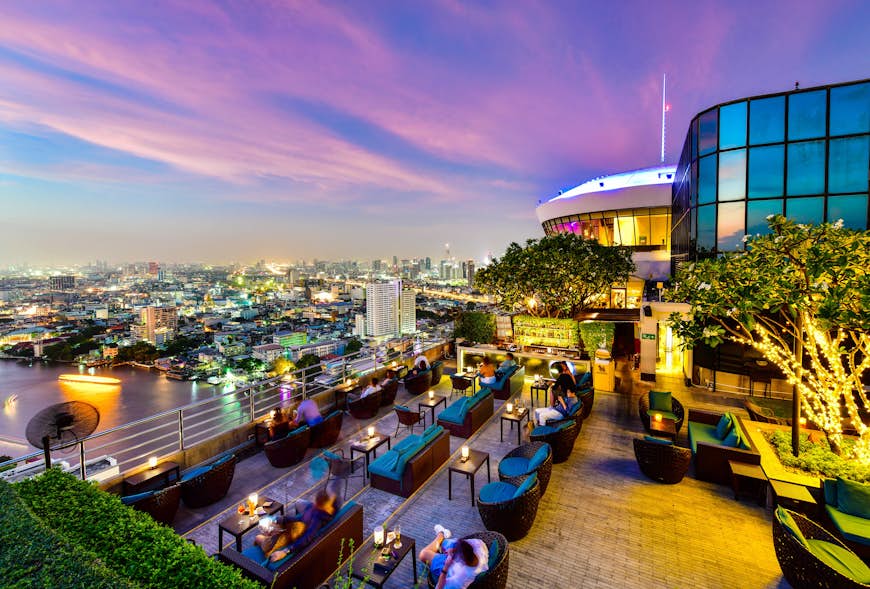 A restaurant bar at dusk with the view of the Bangkok cityscape behind including the river at the Three Sixty Lounge of Millennium Hilton Bangkok Hotel in Bangkok, Thailand