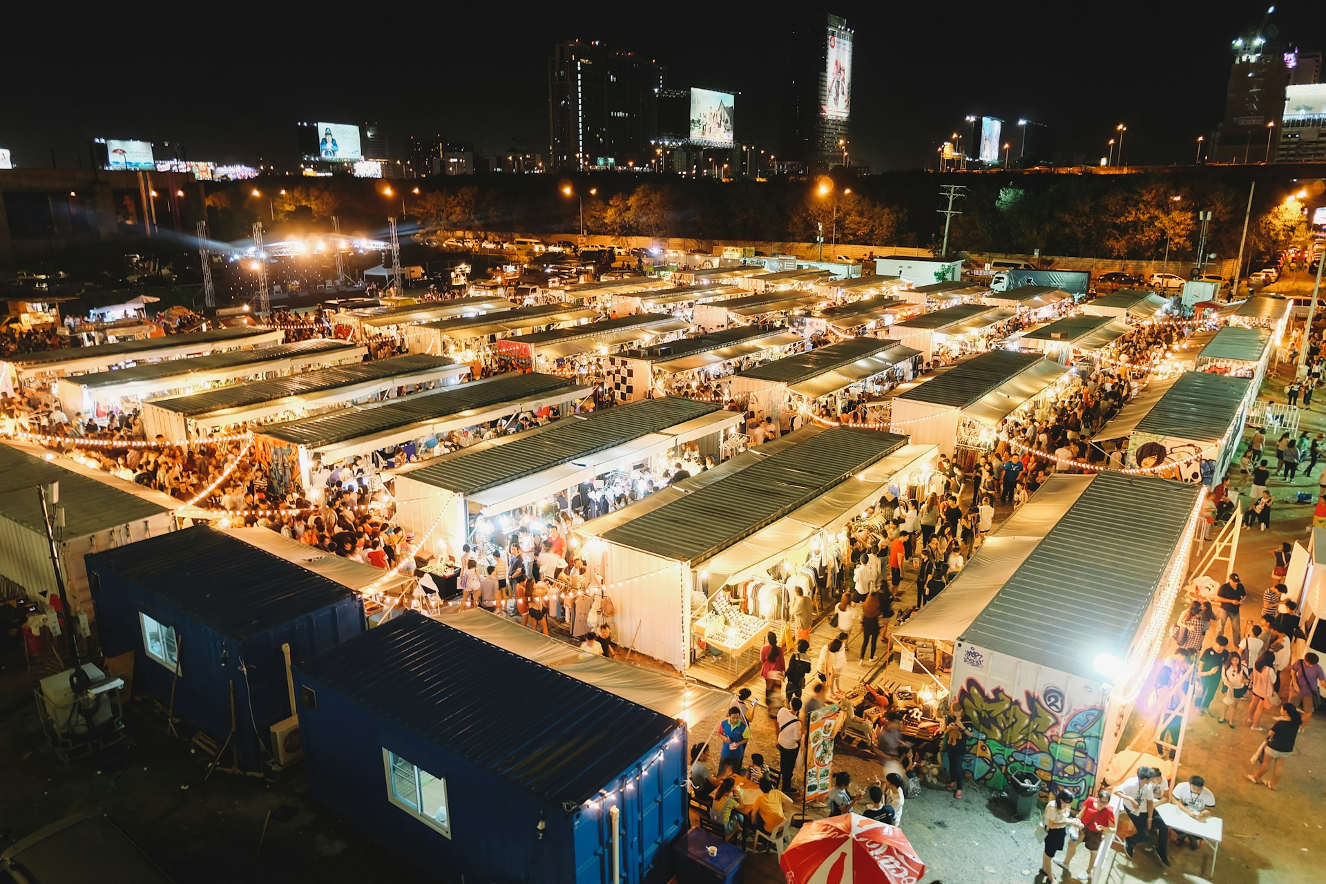 As seen from a vantage point, the stalls of Artbox Night Market in Bangkok glow with light as vendors sell their wares. 