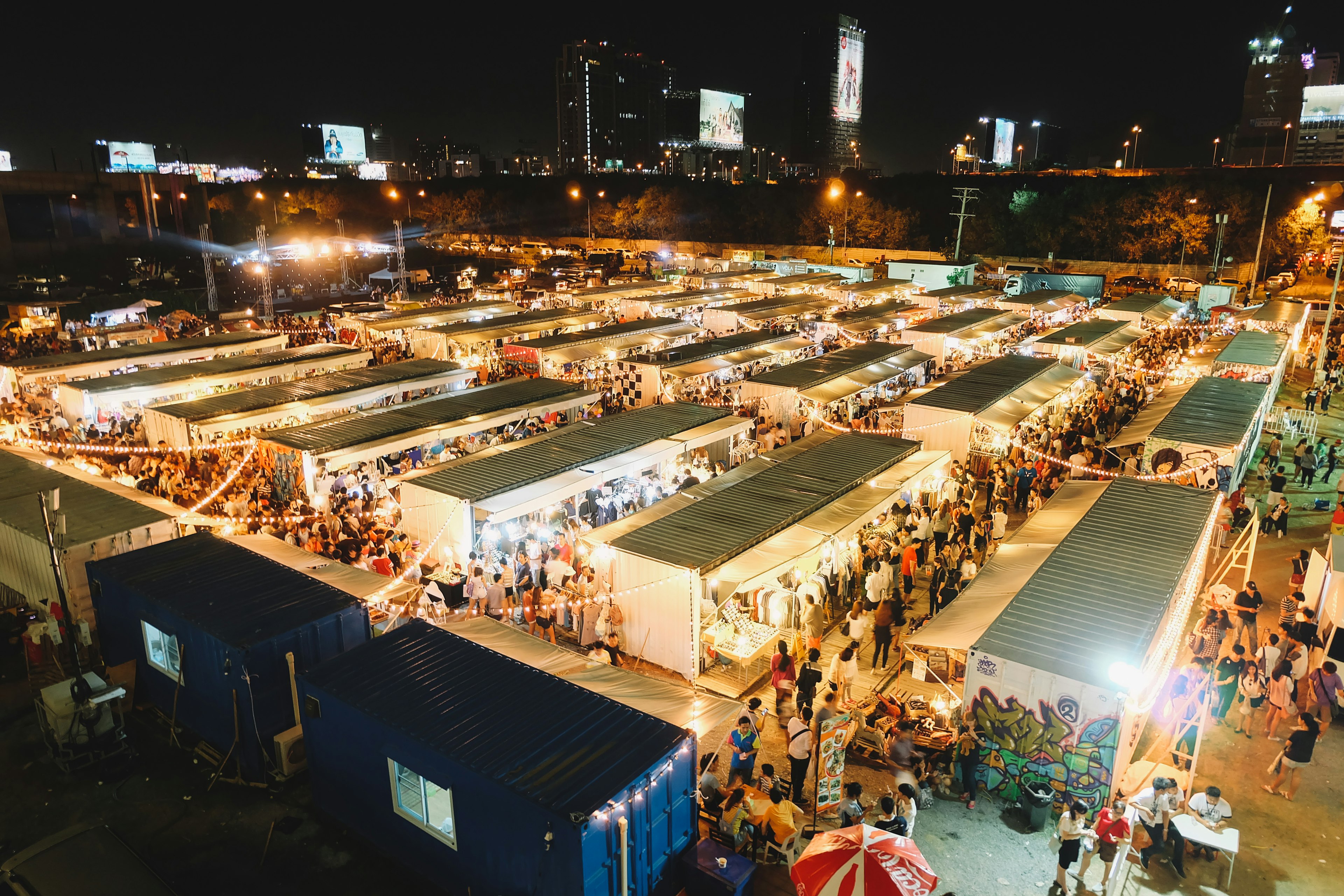 As seen from a vantage point, the stalls of Artbox Night Market in Bangkok glow with light as vendors sell their wares.