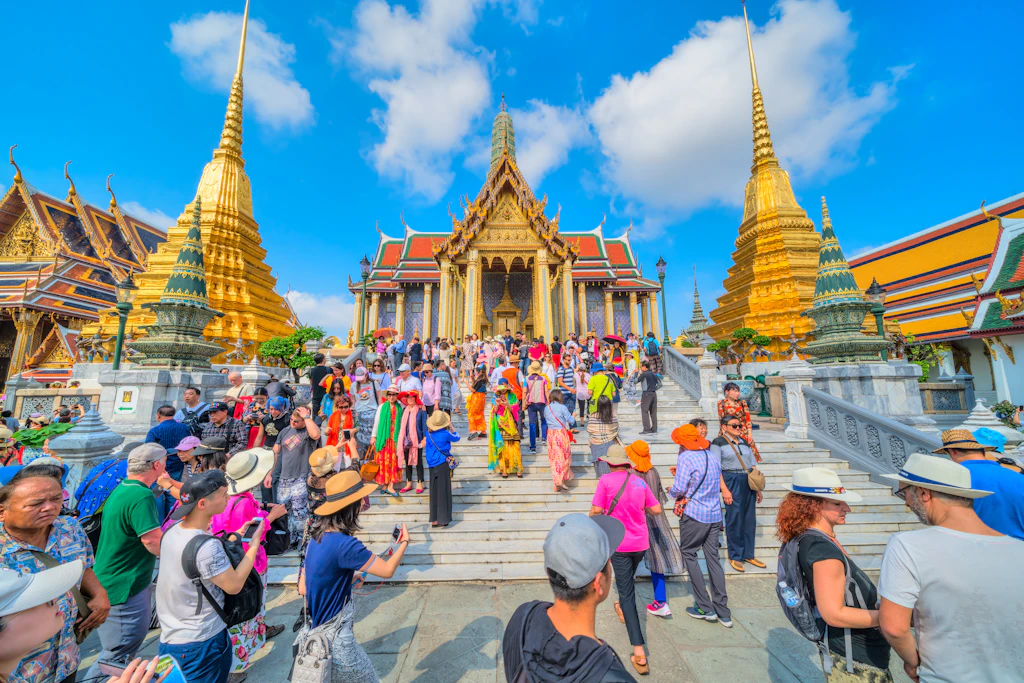 People mill around the complex of the Grand Palace in Bangkok as its golden spires pierce the blue skies.