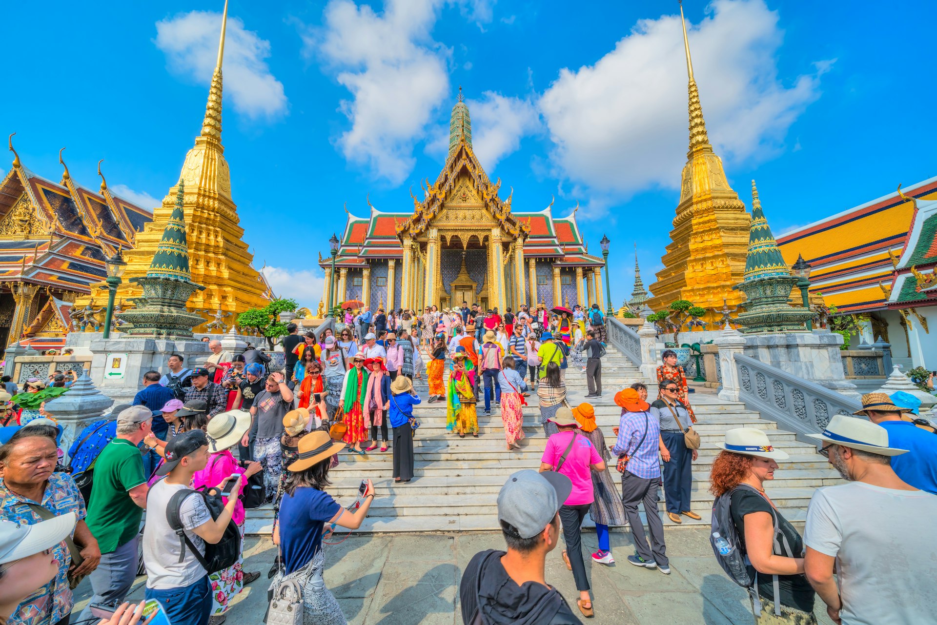 Tourists visiting the Wat Phra Kaew, Temple of the Emerald Buddha, and Grand Palace complex with the golden stupa rising in the background.