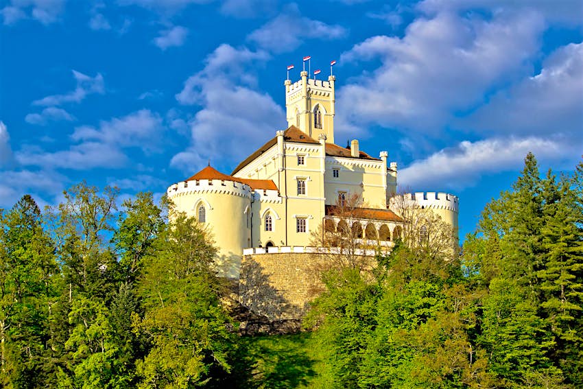 Un château en pierre blanche avec une tour centrale s'élevant au-dessus du reste, et des toits de tuiles rouges