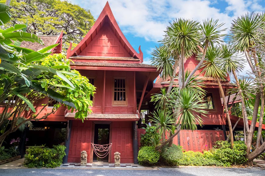 The ochre exterior of the Jim Thompson Museum is Bangkok. The wooden building is slightly hidden behind some trees. 