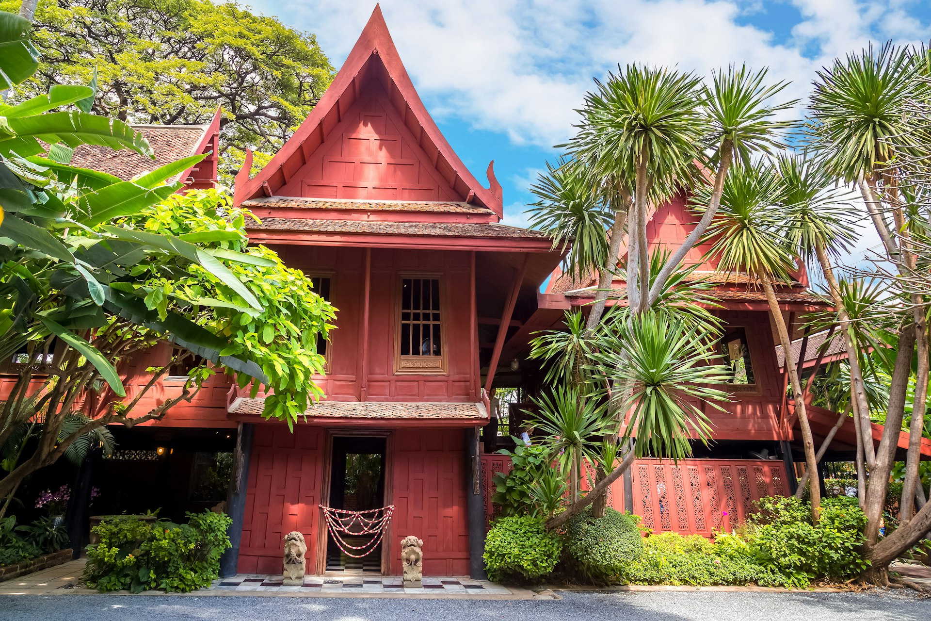 The ochre exterior of the Jim Thompson Museum is Bangkok. The wooden building is slightly hidden behind some trees. 